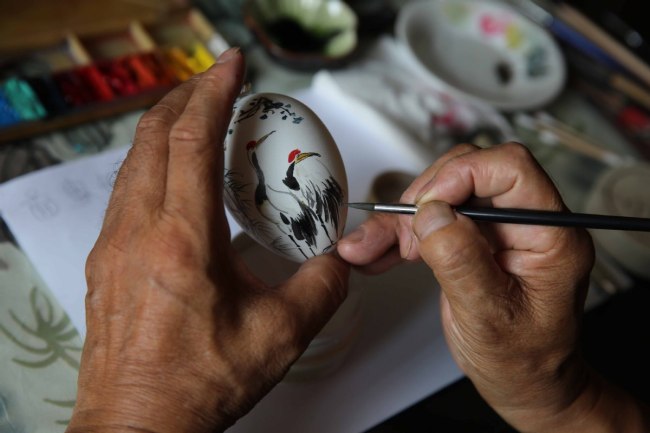 Ο Ρουάν Χαϊλίν ενώ ζωγραφίζει ένα ζευγάρι γερανών πάνω σε ένα αυγό.<br>