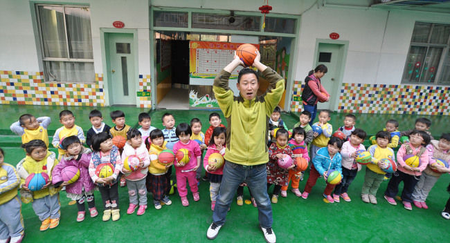 Ο Λιου Μινγκγιάνγκ δείχνει στους μαθητές του νηπιαγωγείου πώς παίζεται το μπάσκετ, στο Τζενγκτζόου της επαρχίας Χενάν. (φωτογραφία/ VCG)