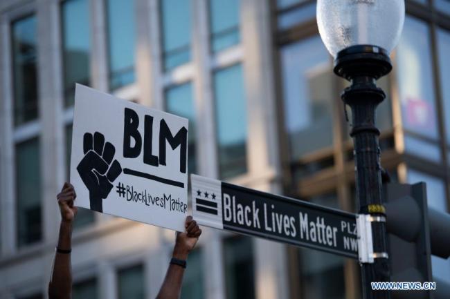 Ένας διαδηλωτής κρατάει μια πινακίδα κοντά στον Λευκό Οίκο στην Ουάσινγκτον, στις Ηνωμένες Πολιτείες, στις 8 Ιουνίου 2020. Στις 25 Μαΐου, ο Αφροαμερικανός Τζορτζ Φλόιντ πέθανε όταν ένας λευκός αστυνομικός γονάτισε πάνω στο λαιμό του για σχεδόν εννέα λεπτά. Ο θάνατός του προκάλεσε παρατεταμένες διαδηλώσεις μεγάλης κλίμακας κατά του ρατσισμού και της αστυνομικής βίας σε όλες τις Ηνωμένες Πολιτείες. Οι εθνοτικές μειονότητες στις Ηνωμένες Πολιτείες αντιμετωπίζουν φυλετικές διακρίσεις και ο ρατσισμός υπάρχει με έναν ολοκληρωμένο, συστηματικό και συνεχή τρόπο, σύμφωνα με την Έκθεση για τις Παραβιάσεις των Ανθρωπίνων Δικαιωμάτων στις Ηνωμένες Πολιτείες το 2020, η οποία κυκλοφόρησε από το Γραφείο Πληροφοριών του Κρατικού Συμβουλίου της Κίνας την Τετάρτη. (φωτογραφία: Xinhua)
