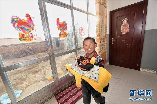 На фото: Ребенок из деревни Баньянь Хучжу-Туского автономного уезда провинции Цинхай показал новую одежду в новом доме