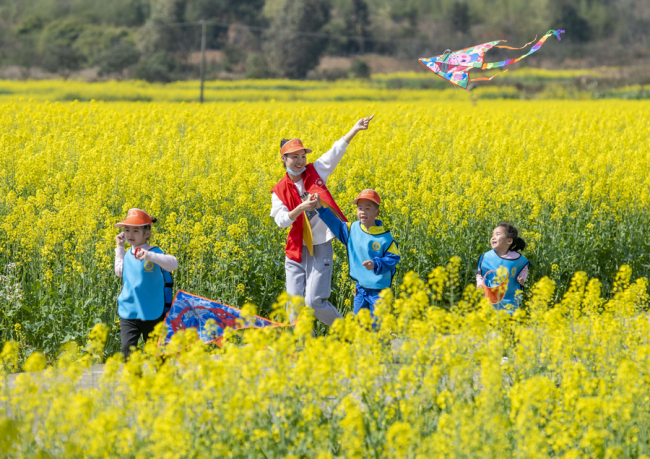 Učitelé a děti společně pouští draky na květinové základně ve vesnici Lianghekou (Liang-che-kchou) v okresu Daoxian (Tao-sien) ve městě Yongzhou (Jung-čou) v čínské provincii Hunan (Chu-nan). Mateřská školka uspořádala hodinu v řepkové poli, aby děti pocítily kouzlo jara. [Fotografie: Jiang Keqing (Ťiang Kche-čching) / deník China Daily]