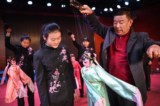 Ένας συνεχιστής της εθνικής άυλης πολιτιστικής κληρονομιάς της μαριονέτας Χεγιάνγκ, δείχνει πώς κινείται μια μαριονέτα σε νέους μαθητές, στις 4 Μαρτίου 2022. [Φωτογραφία/Xinhua]