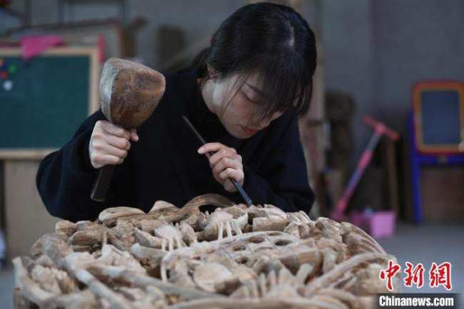 Η Τσεν Τζια δημιουργεί ένα έργο τέχνης ξυλογλυπτικής. (Chinanews.com/Chen Chuhong)