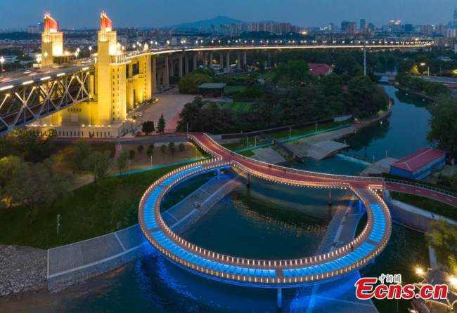 Ένας νεόκτιστος στρογγυλός γυάλινος διάδρομος που δημιουργήθηκε δίπλα στη γέφυρα του ποταμού Γιανγκτζέ του Ναντζίνγκ, φωτίζεται με διάφορα χρώματα τις νύχτες στην επαρχία Τζιανγκσού της ανατολικής Κίνας. (Φωτογραφία: China News Service)