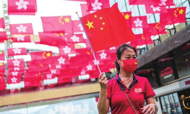 Žena třímající čínskou národní vlajku a stojící pod vlajkami Číny a Zvláštní administrativní oblasti Hongkongu při spojených oslavách stého výročí založení Čínské komunistické strany s oslavami 24. výročí návratu Hongkongu k Číně. Photo: IC