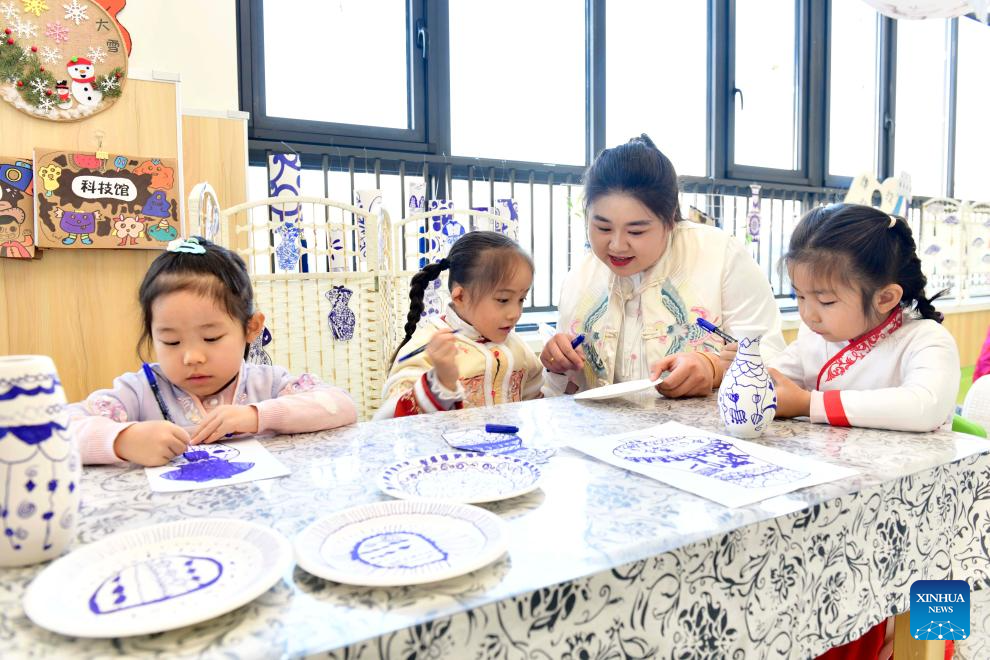 Η δασκάλα Λι Τιενγί δείχνει στα παιδιά πώς να ζωγραφίζουν σχέδια για μπλε και λευκή πορσελάνη σε χαρτί στο νηπιαγωγείο Σανγουάνγκ στο Τζινάν, στην επαρχία Σανντόνγκ της ανατολικής Κίνας, στις 29 Νοεμβρίου 2023. (Xinhua/Guo Xulei)